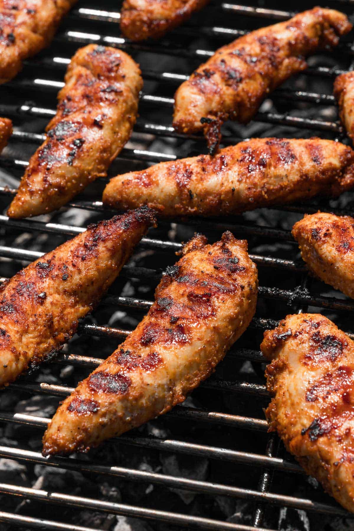 side view of marinated chicken tenders cooking on a grill.
