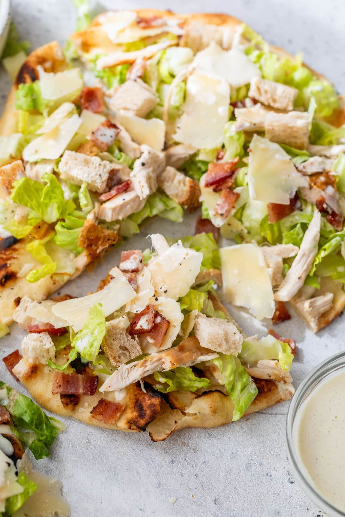 overhead view of a sliced Caesar salad pizza topped with shaved parmesan.