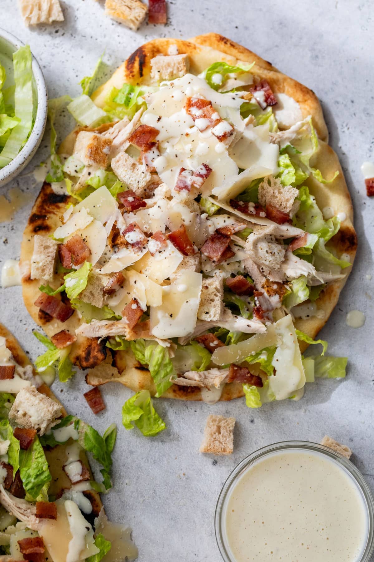 overhead view of a Caesar salad pizza topped with shaved parmesan and bacon.
