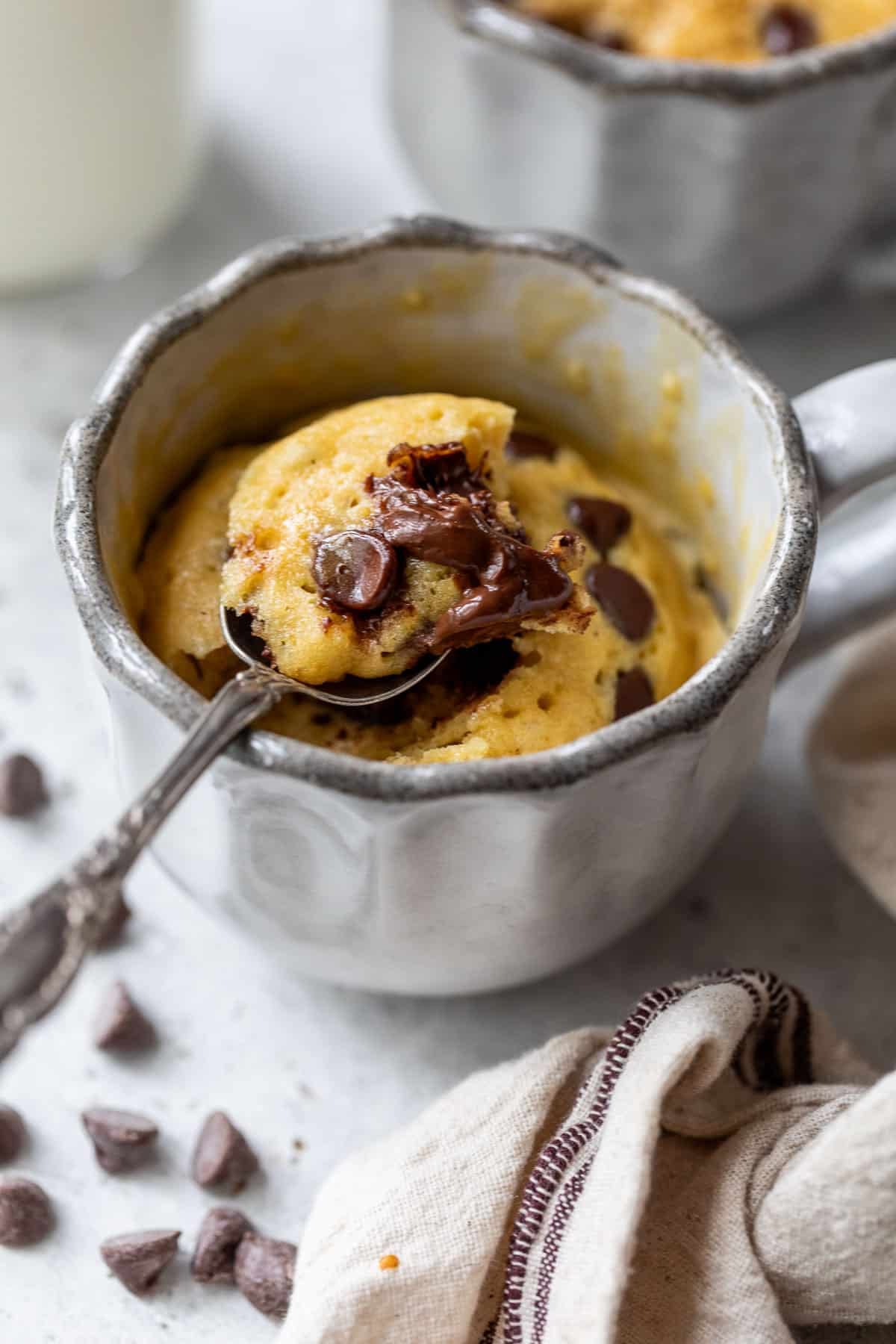 side view of a spoon lifting a scoop of a chocolate chip mug cake from a mug.