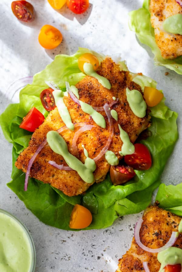 overhead view of cooked paleo cod in a lettuce cup with green avocado sauce drizzled on top.