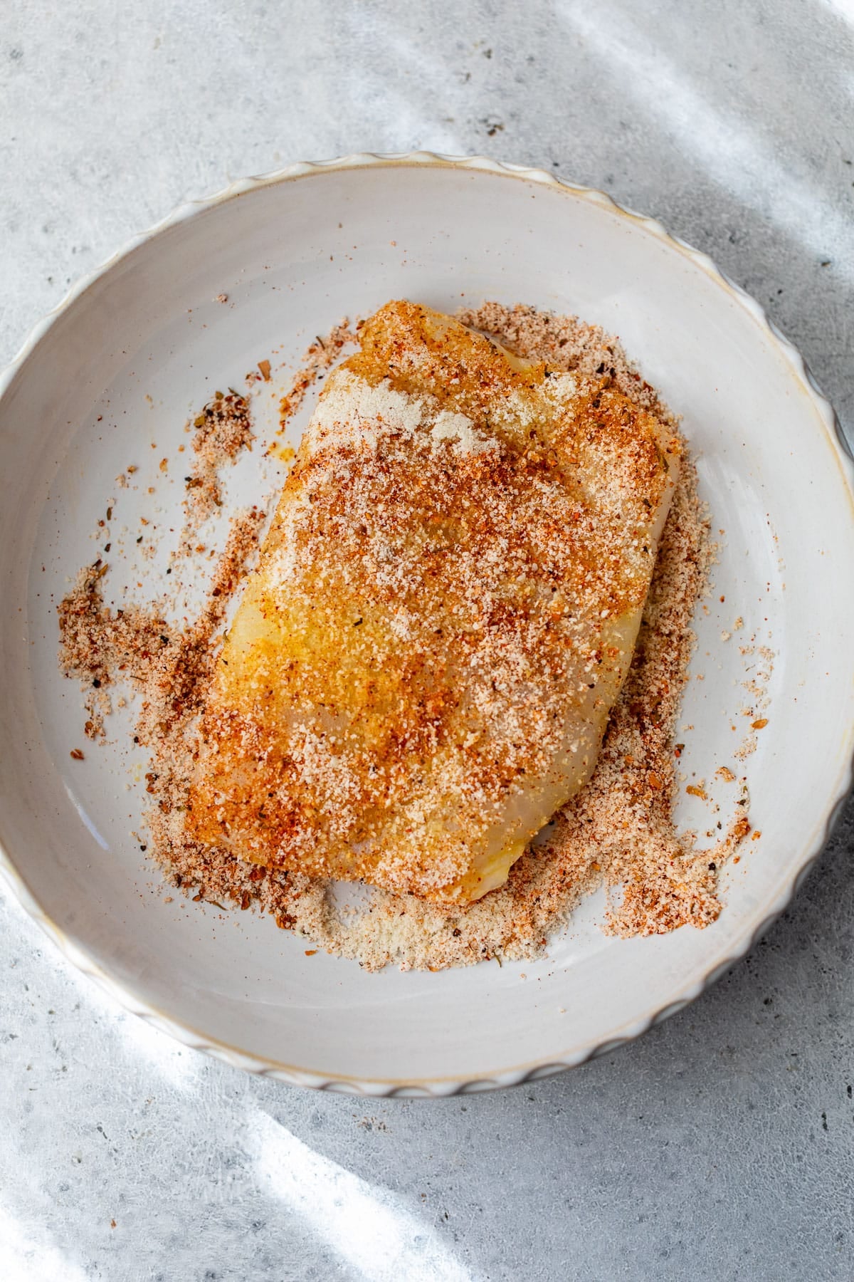 overhead view of a piece of cod being dredged in an almond flour coating on a plate.