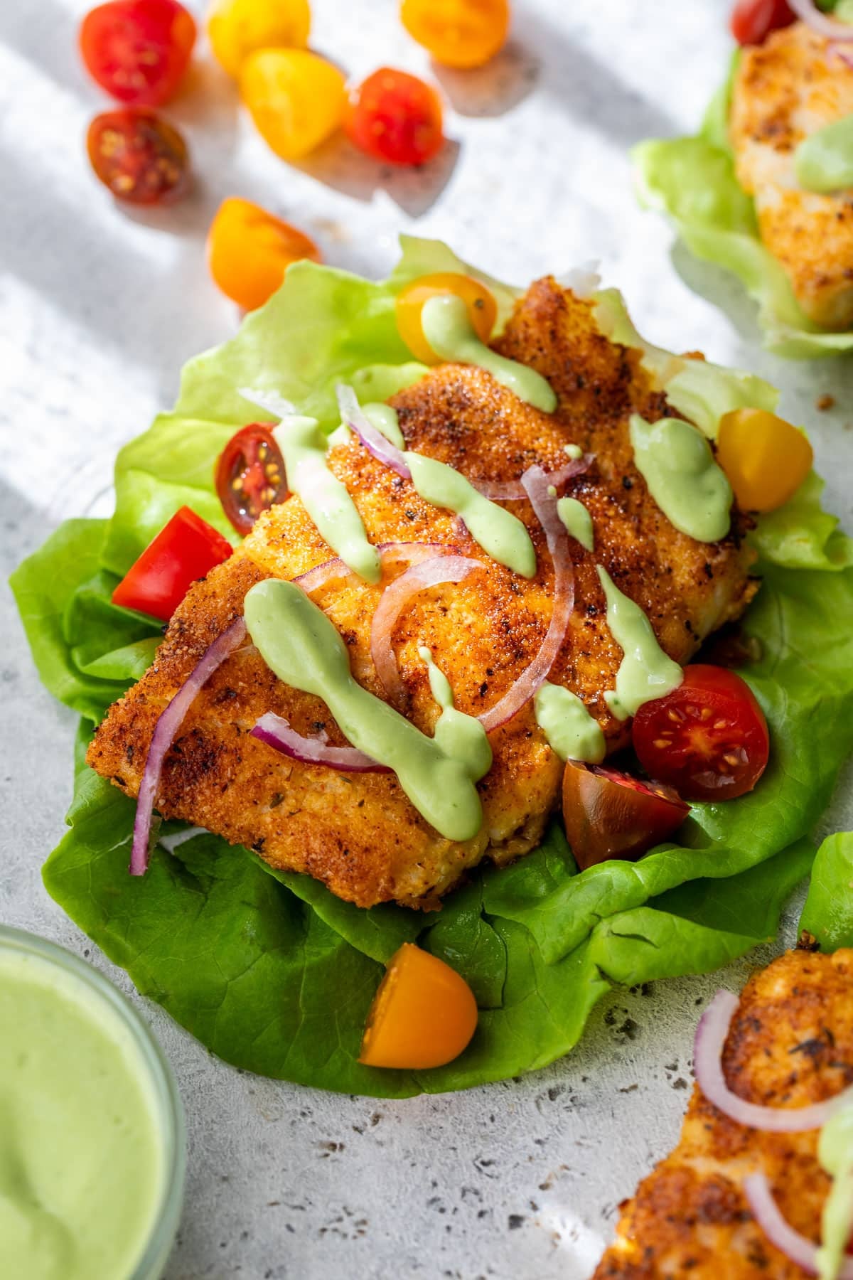 overhead view of cooked paleo cod in a lettuce cup with green avocado sauce drizzled on top.