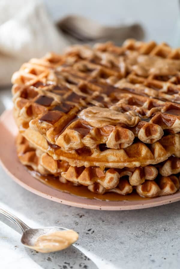 side view of a stack of peanut butter waffles topped with maple syrup and peanut butter on a plate.