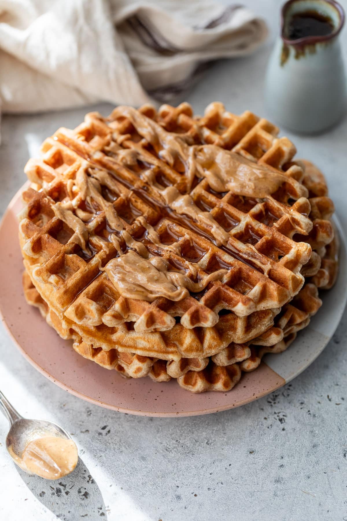 overhead view of a stack of peanut butter waffles topped with maple syrup and peanut butter on a plate.