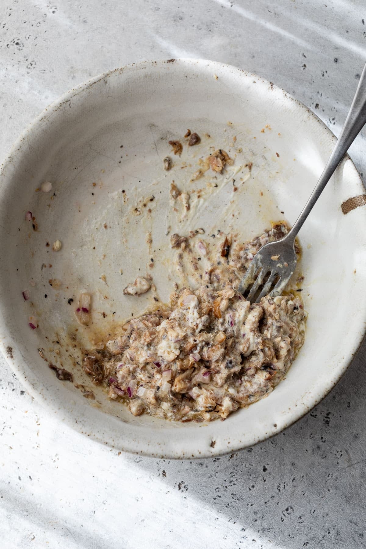 overhead view of a fork mashing sardines in a bowl.