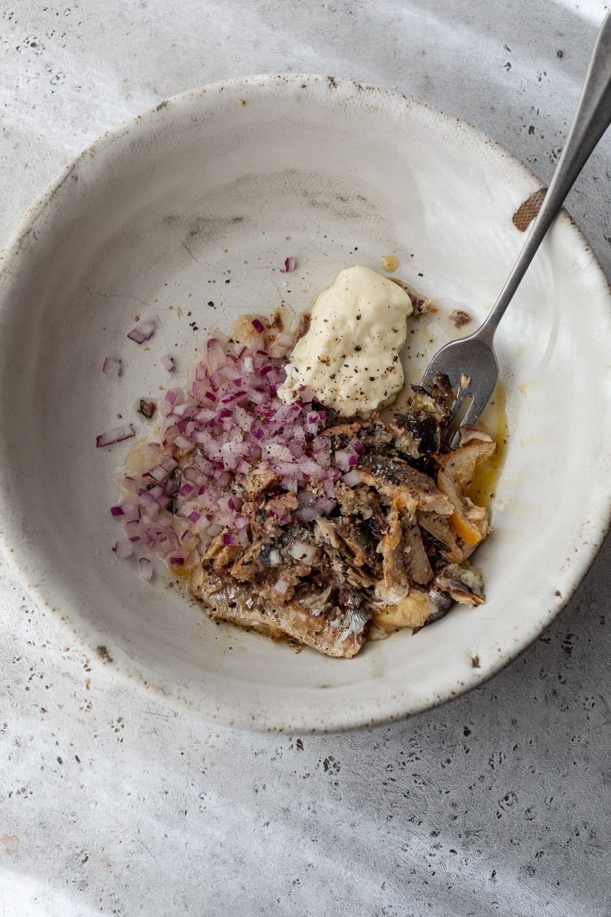 overhead view of a fork mixing the ingredients for sardine salad in a bowl.