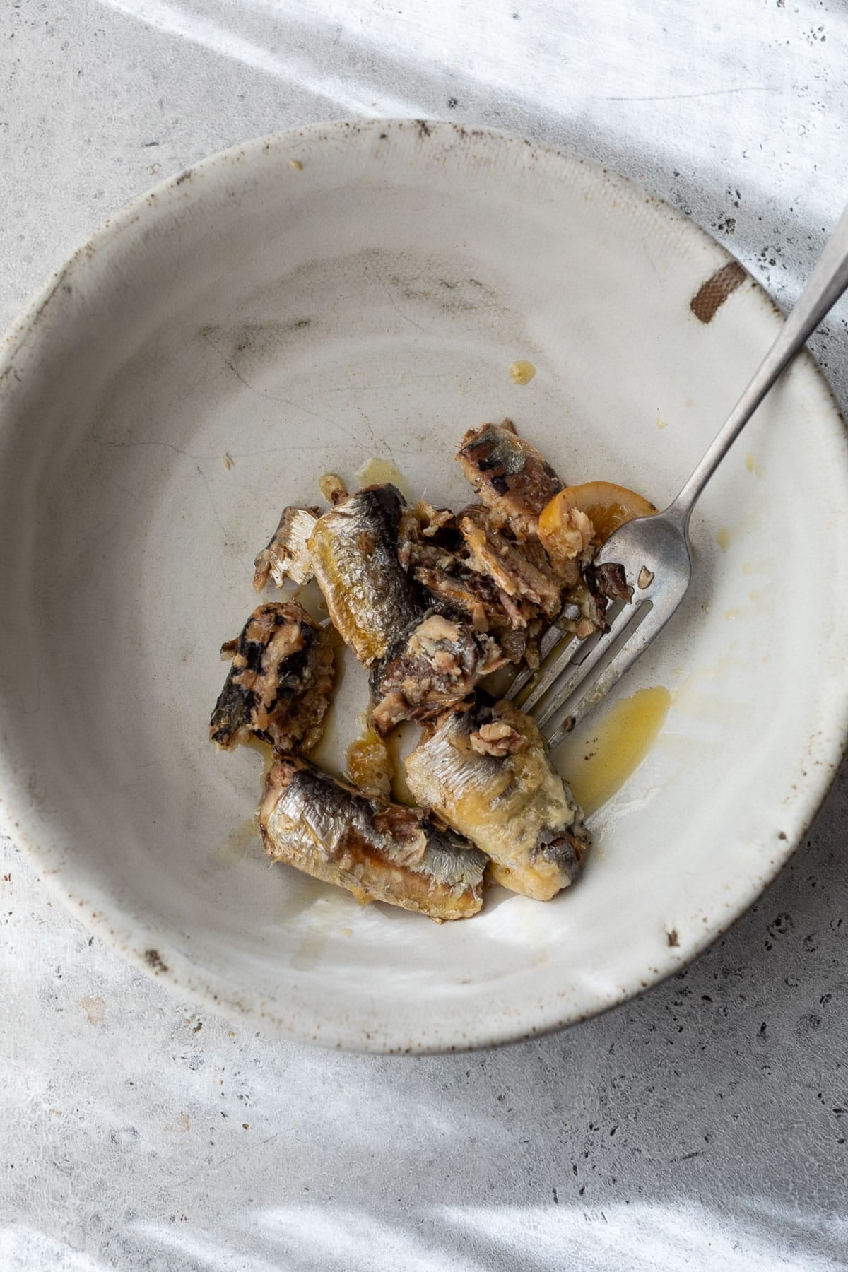 overhead view of a fork mashing sardines in a bowl.