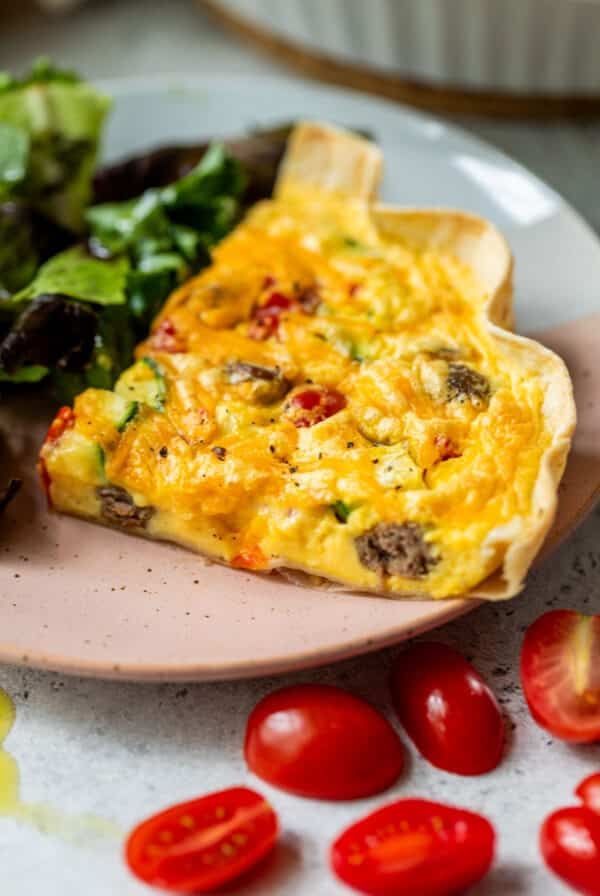 side view of a slice of tortilla quiche next to a salad on a plate.