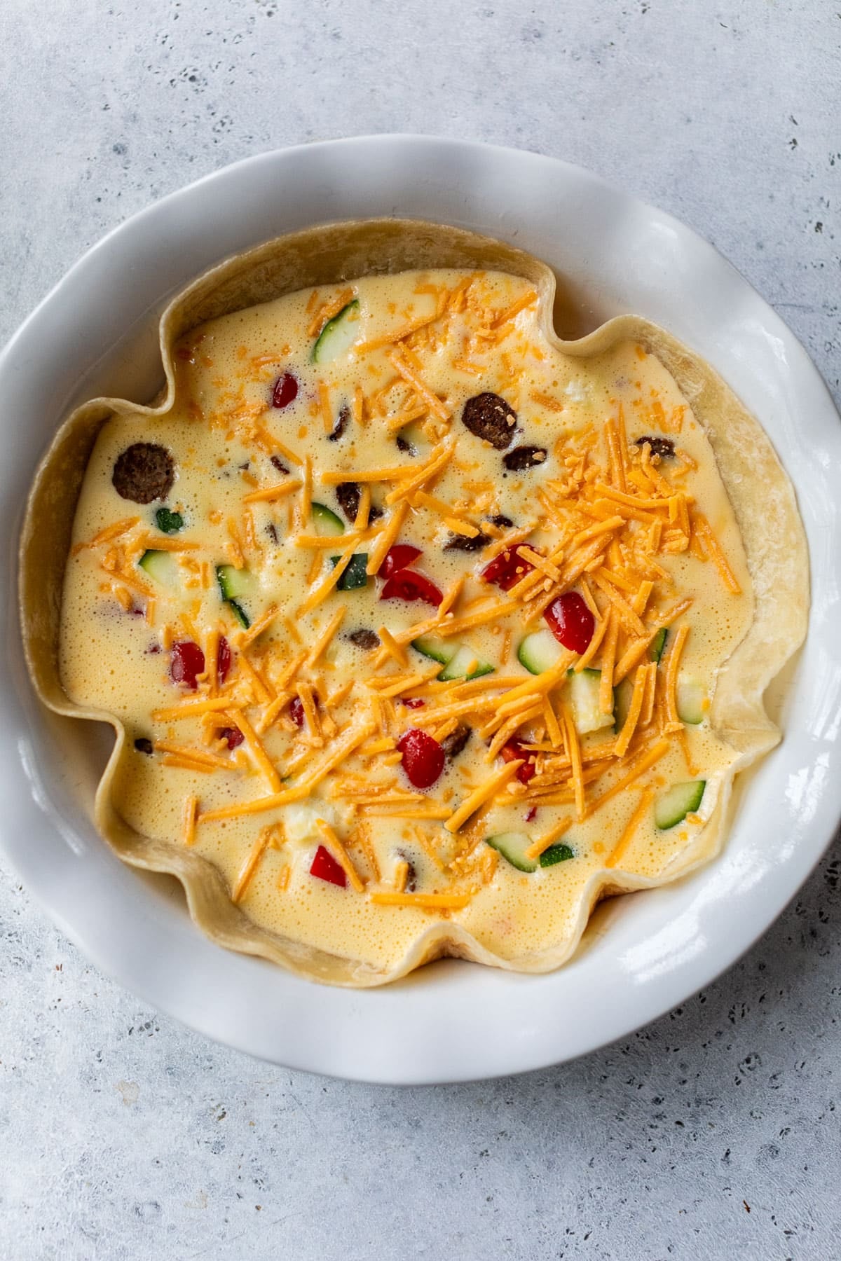 overhead view of an unbaked tortilla quiche in a white pie plate.