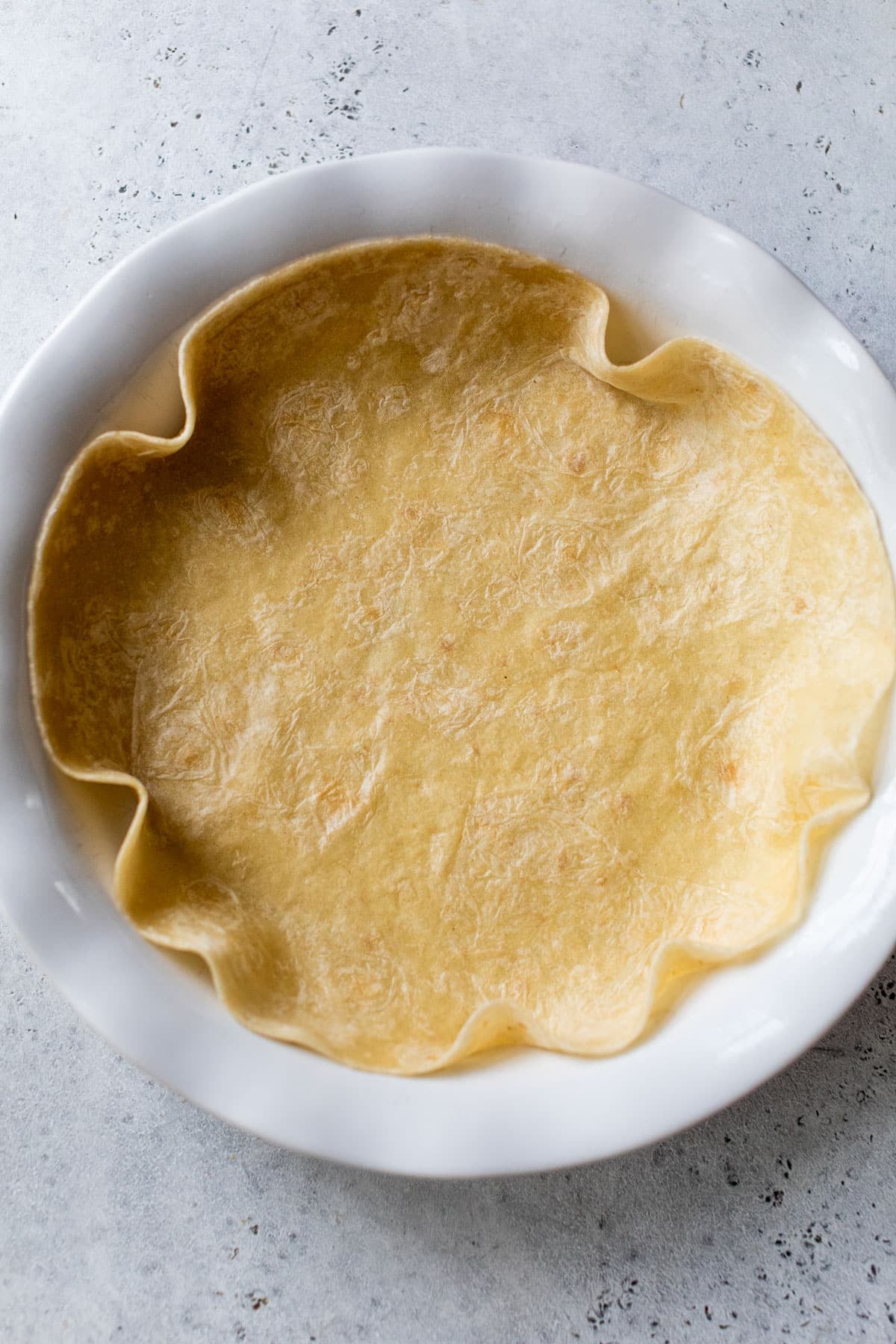 overhead view of a large tortilla pressed into a white pie plate.