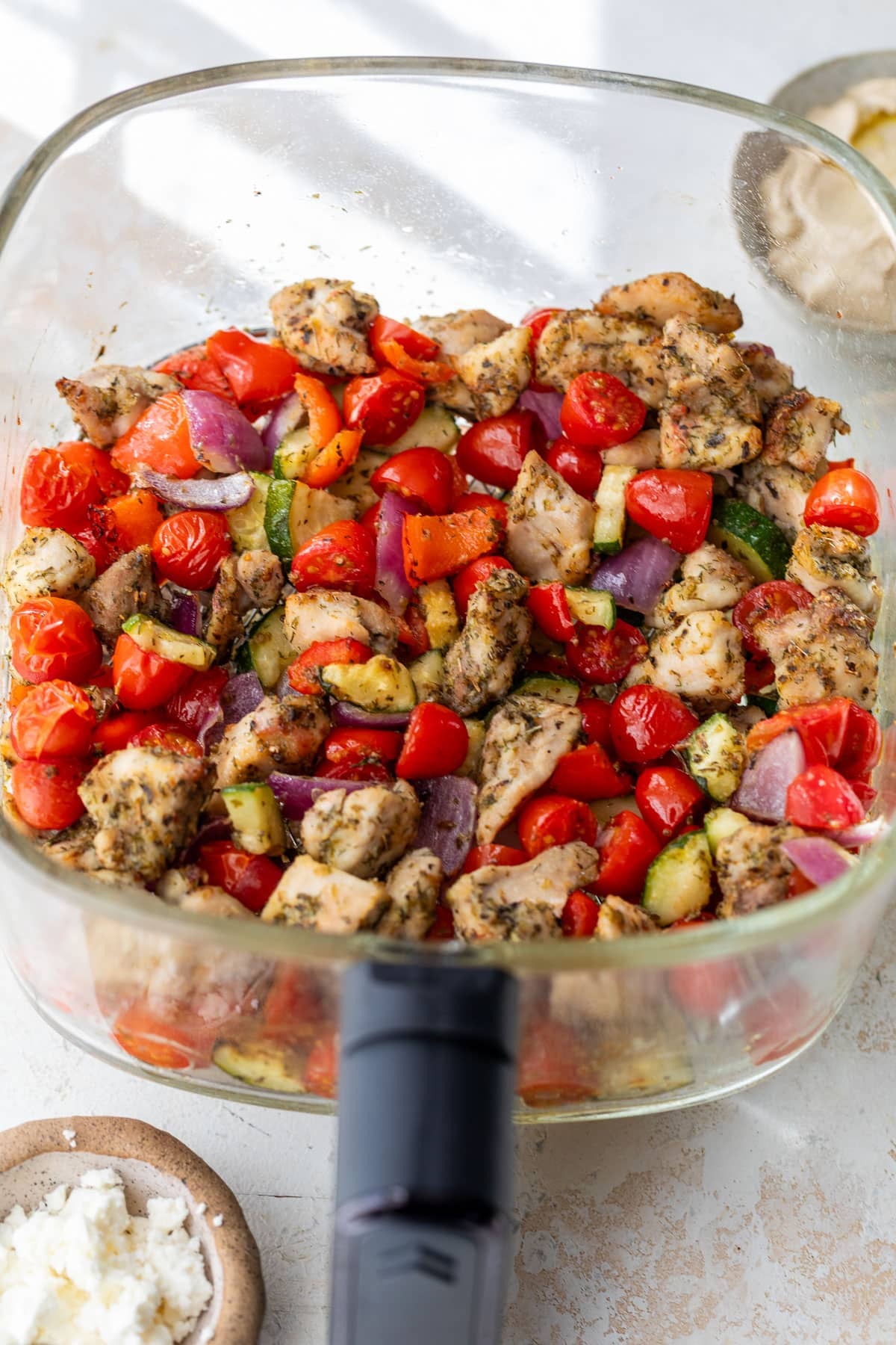side view of the cooked ingredients for air fryer Greek chicken in a glass air fryer basket.