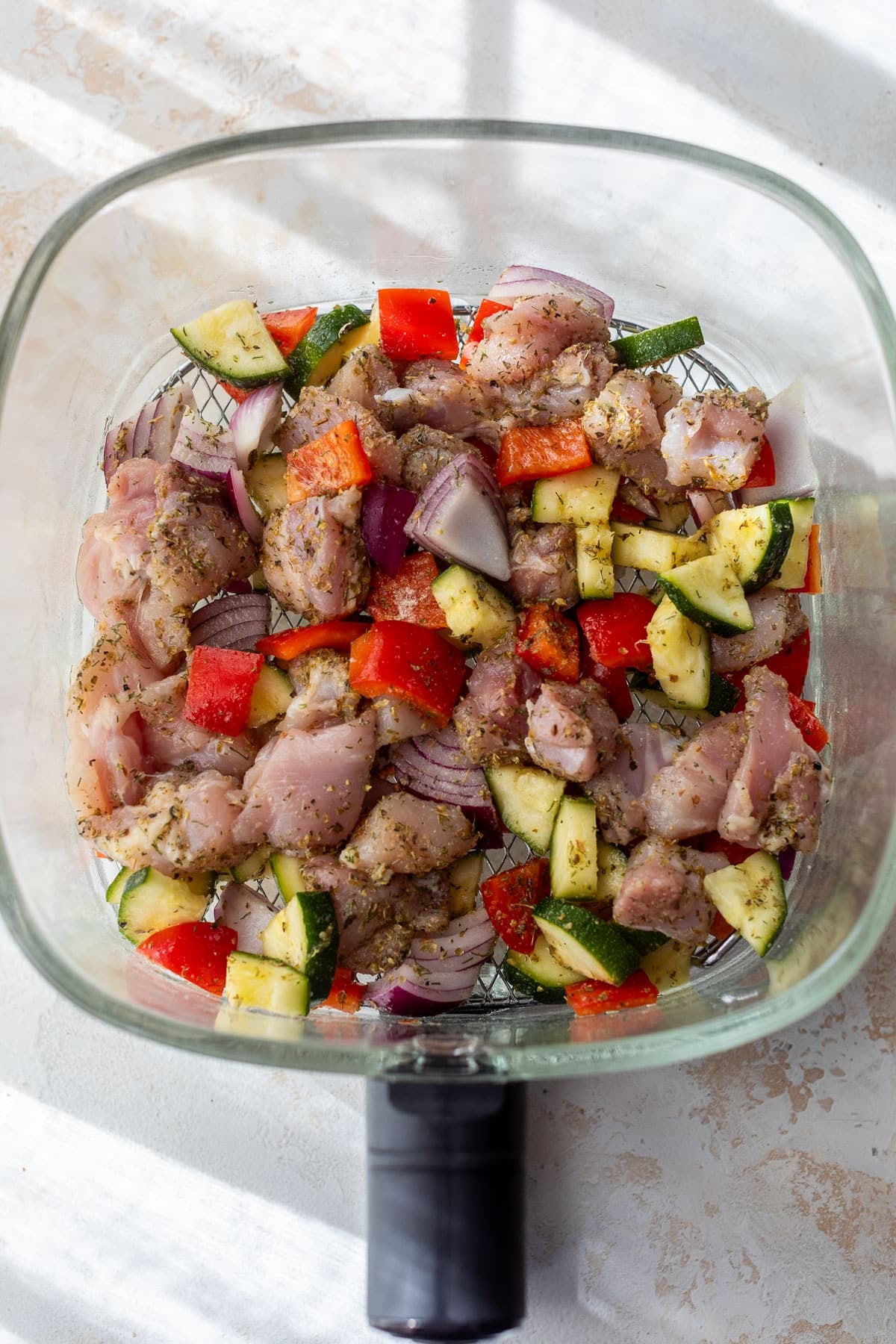 overhead view of the raw ingredients for air fryer Greek chicken in a glass air fryer basket.