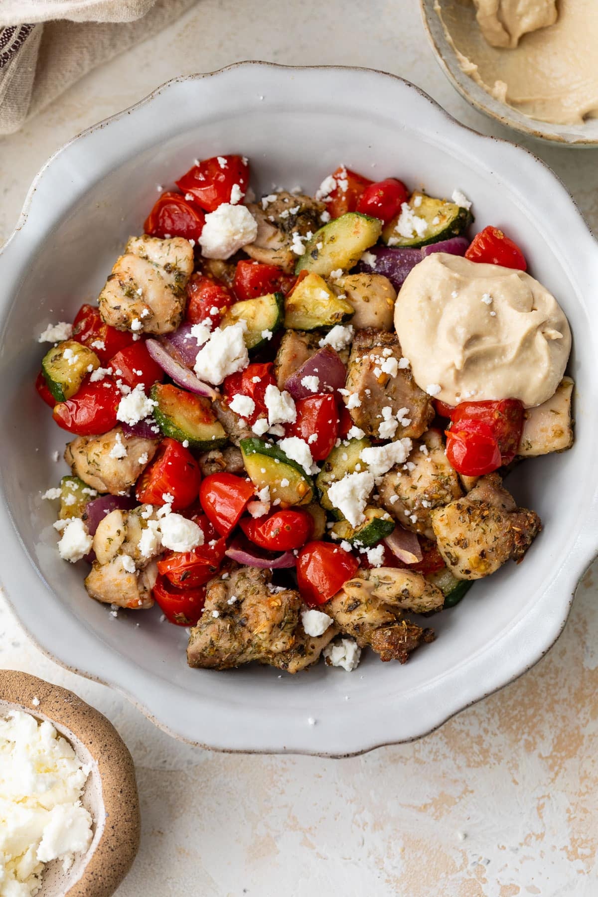 overhead view of air fryer greek chicken and vegetables in a large white bowl.