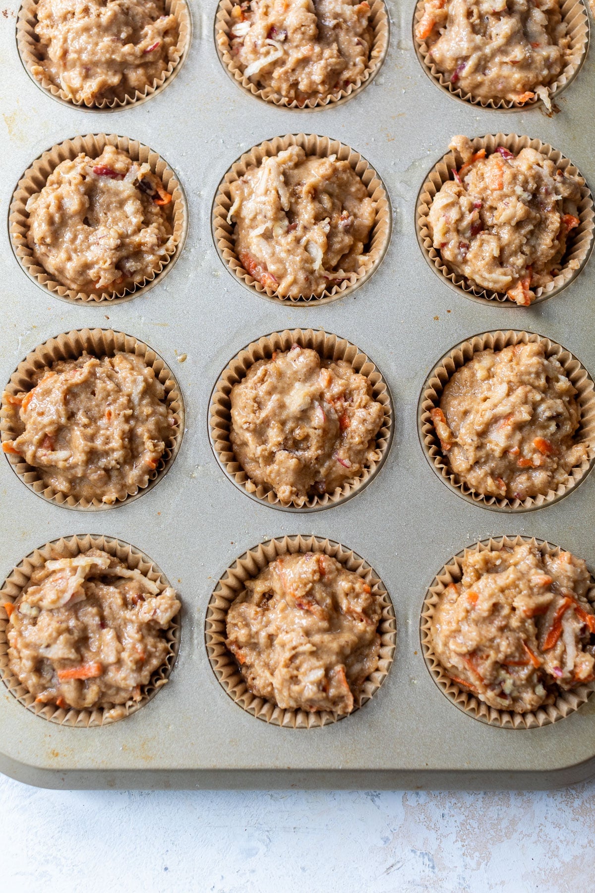 overhead view of unbaked apple carrot muffins in a muffin tin.