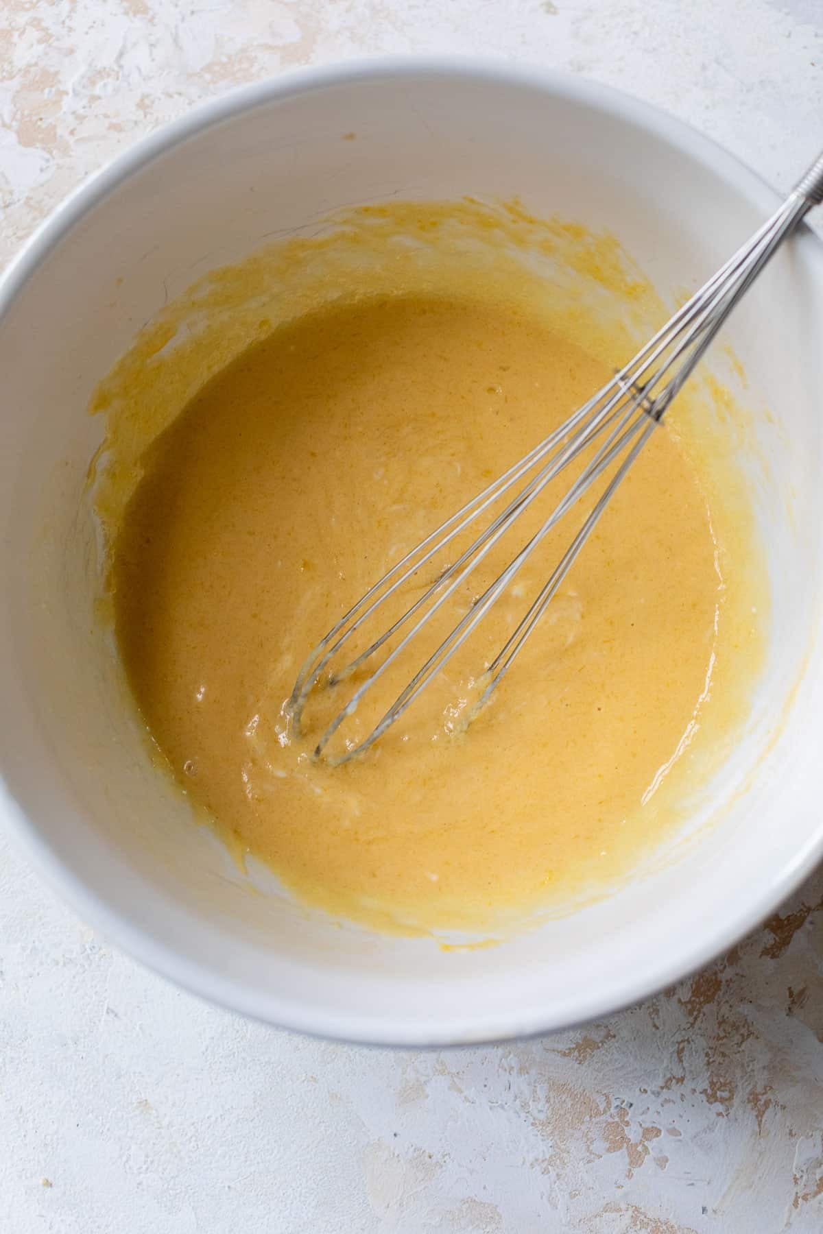 overhead view of a whisk and the wet ingredients for apple carrot muffin batter in a white bowl.
