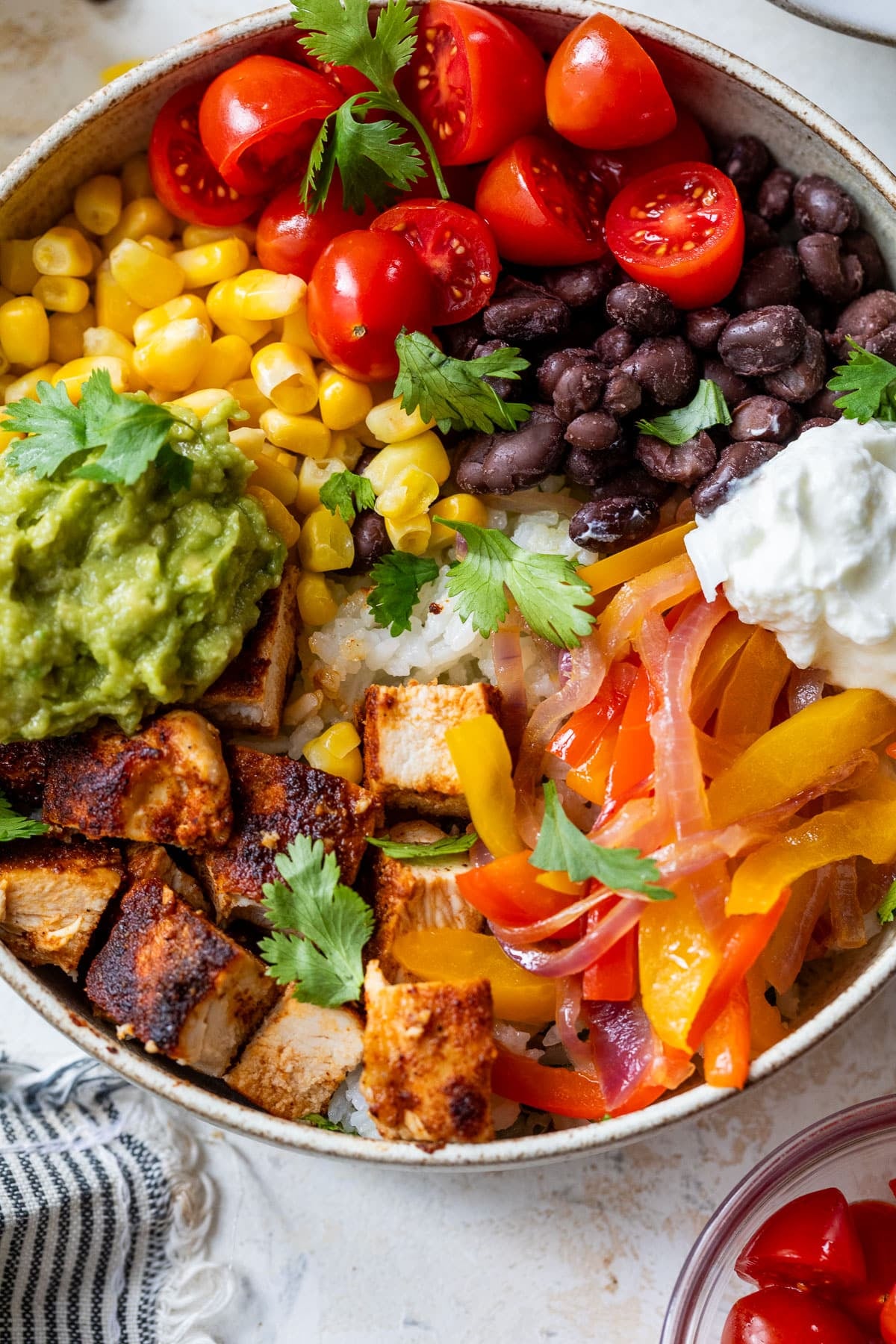 overhead view of a chicken burrito bowl topped with chicken, black beans, corn, tomatoes, and guacamole.