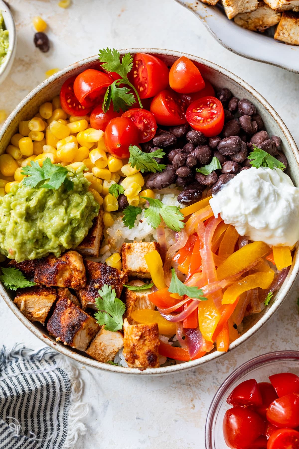 overhead view of a chicken burrito bowl topped with chicken, black beans, corn, tomatoes, and guacamole.