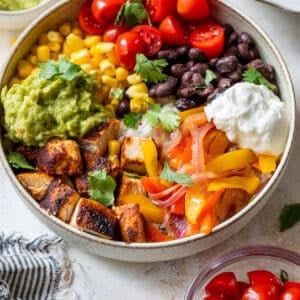 overhead view of a chicken burrito bowl topped with chicken, black beans, corn, tomatoes, and guacamole.