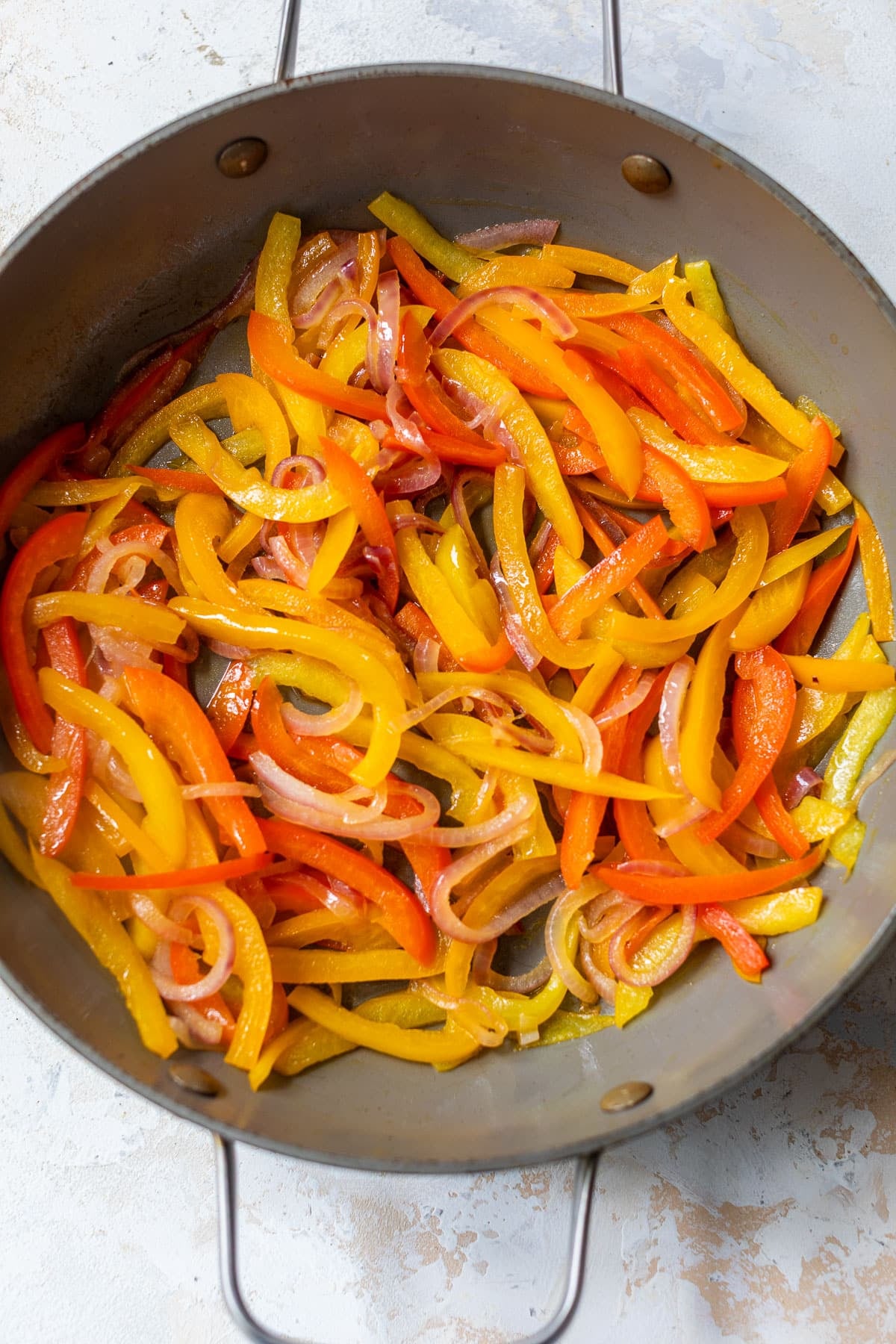 overhead view of sliced onions and bell peppers cooking in a pan.