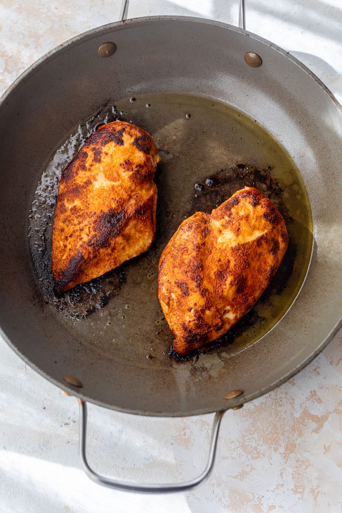 overhead view of 2 blackened-seasoned and cooked chicken breasts in a skillet.