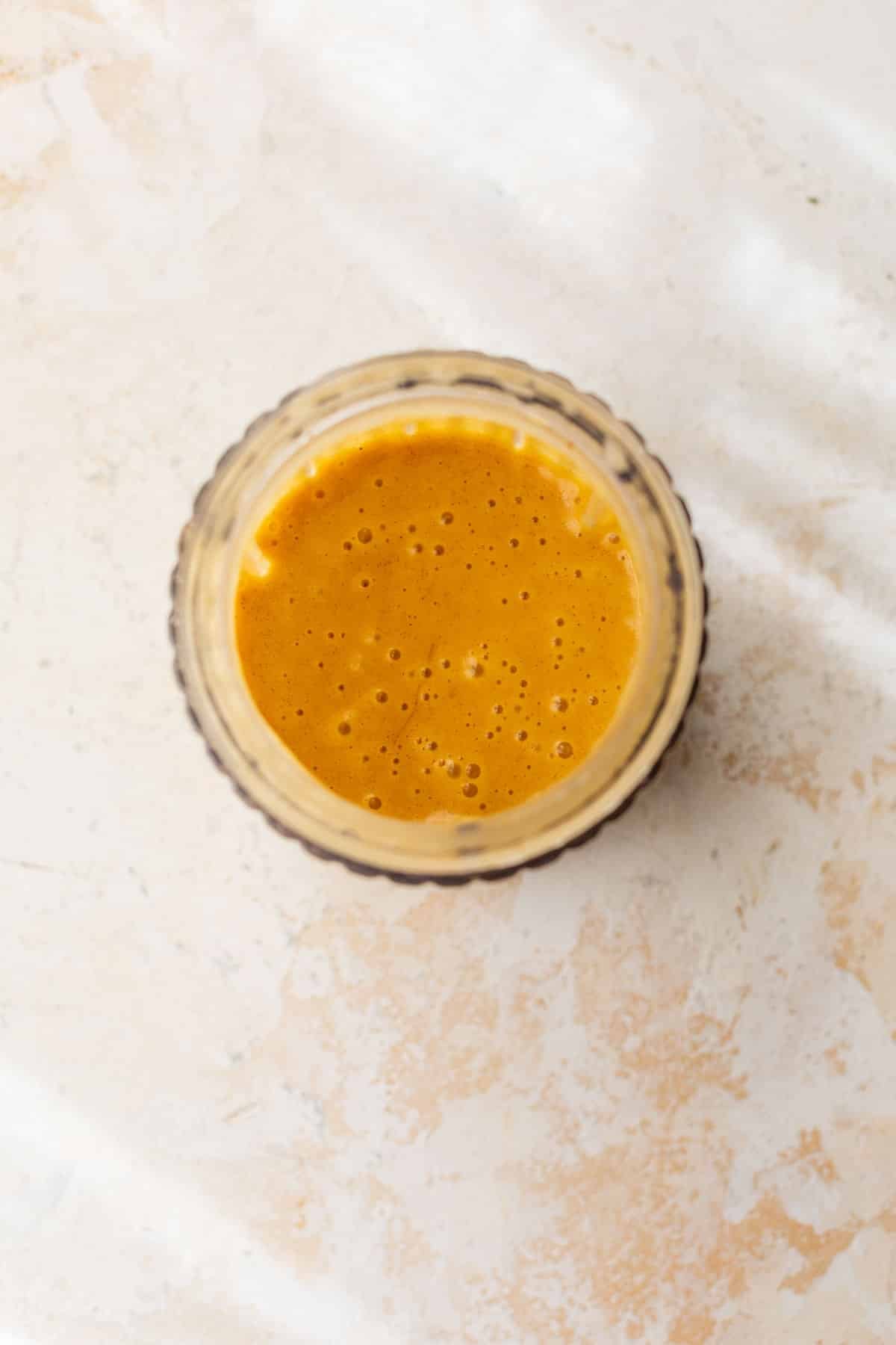 overhead view of a creamy, orange hot honey sauce in a glass cup.