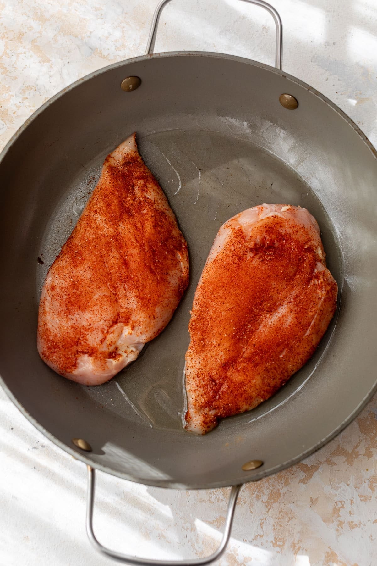 overhead view of 2 blackened-seasoned raw chicken breasts in a skillet.