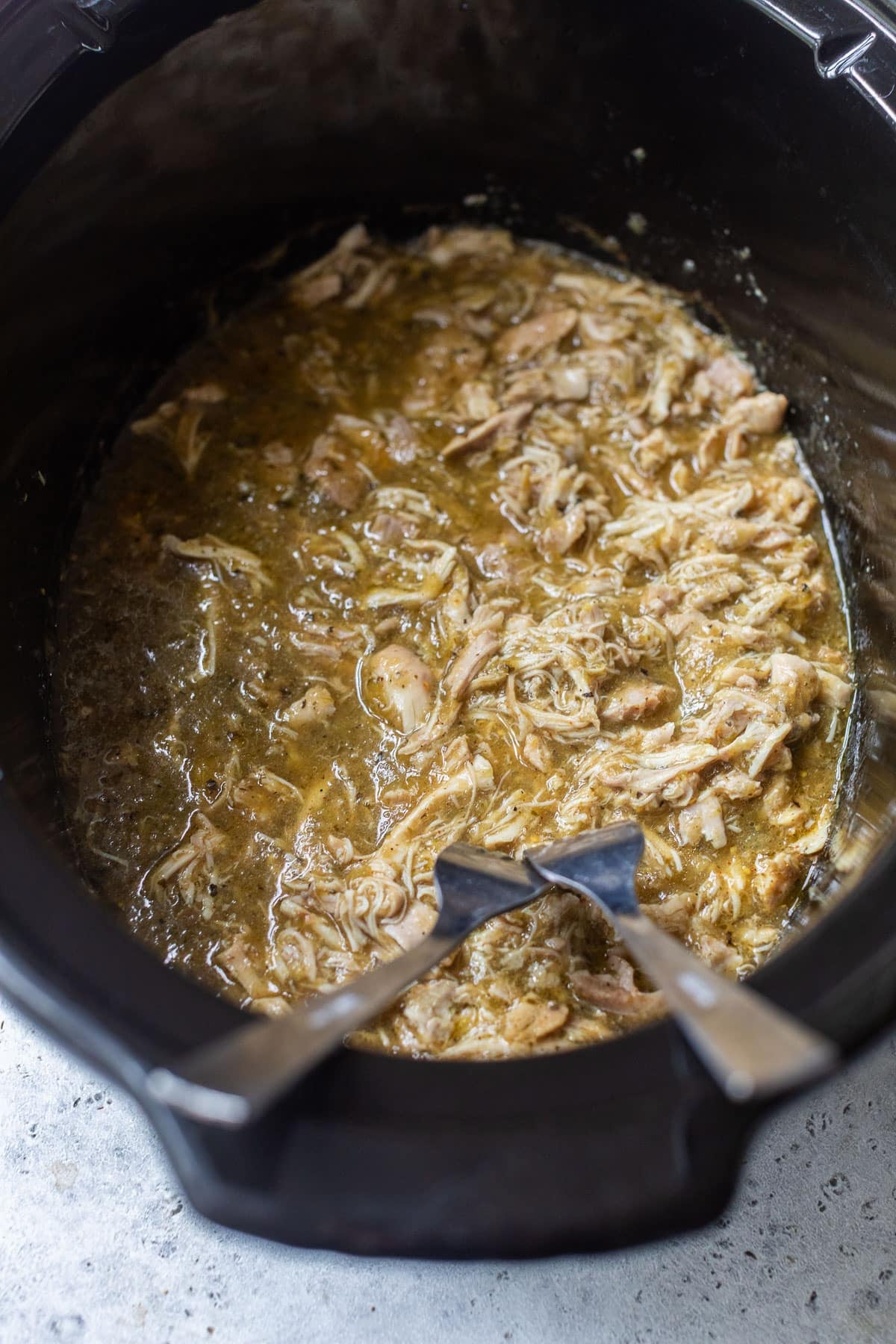 side view of two forks in a crockpot full of salsa verde chicken.