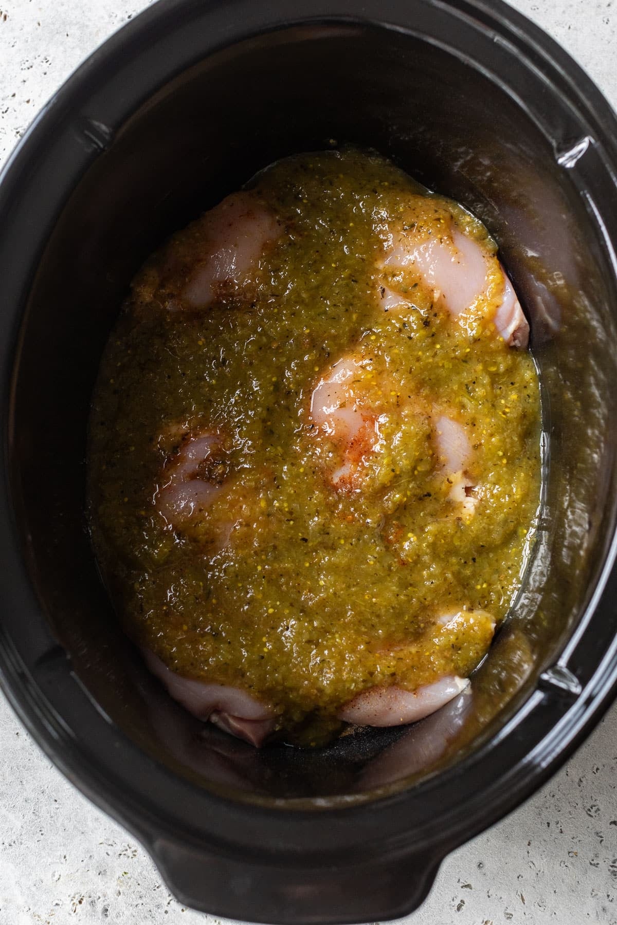 overhead view of raw chicken thighs topped with salsa verde in a crockpot.
