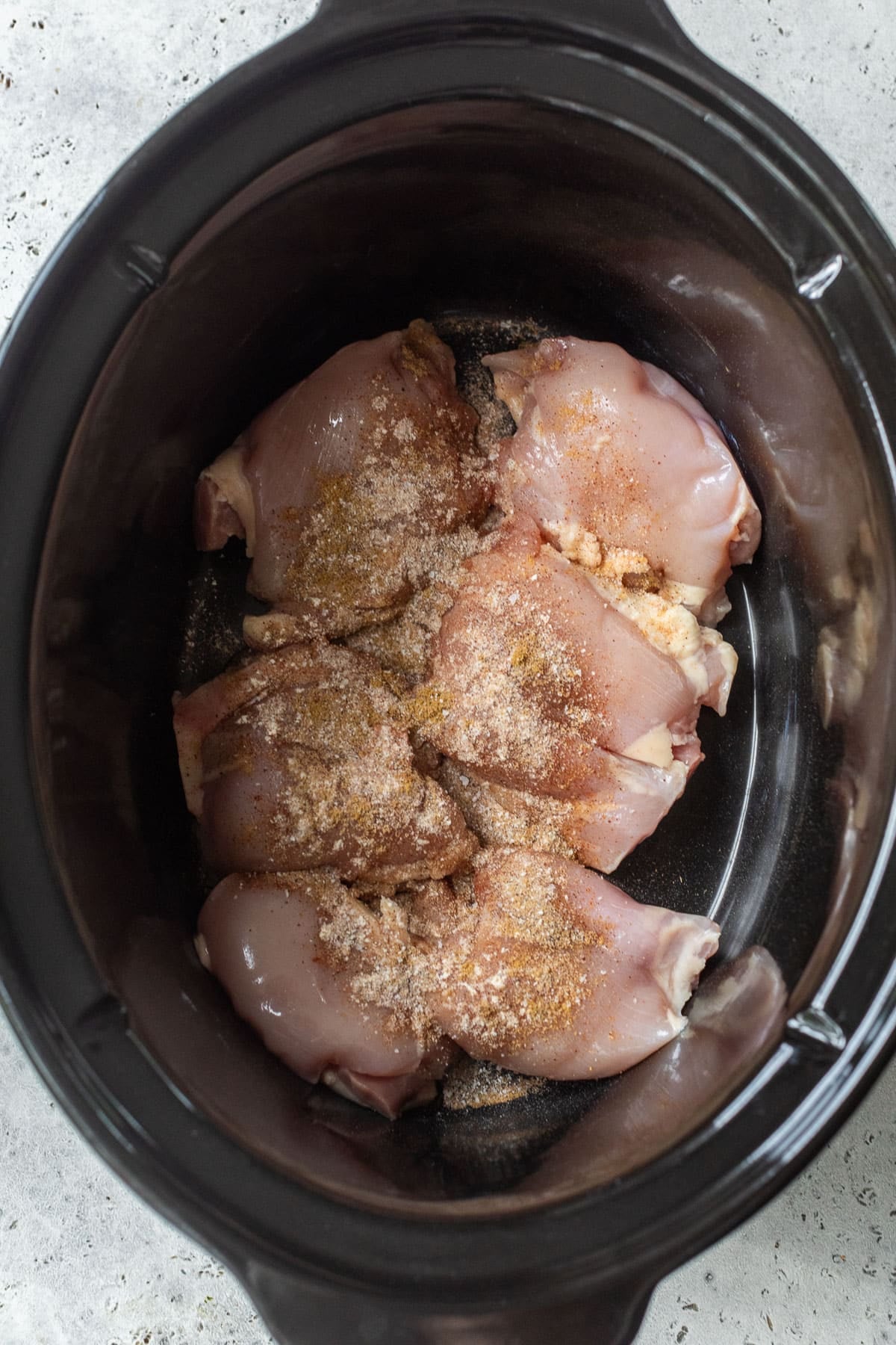 overhead view of raw chicken thighs topped with seasonings in a crockpot.
