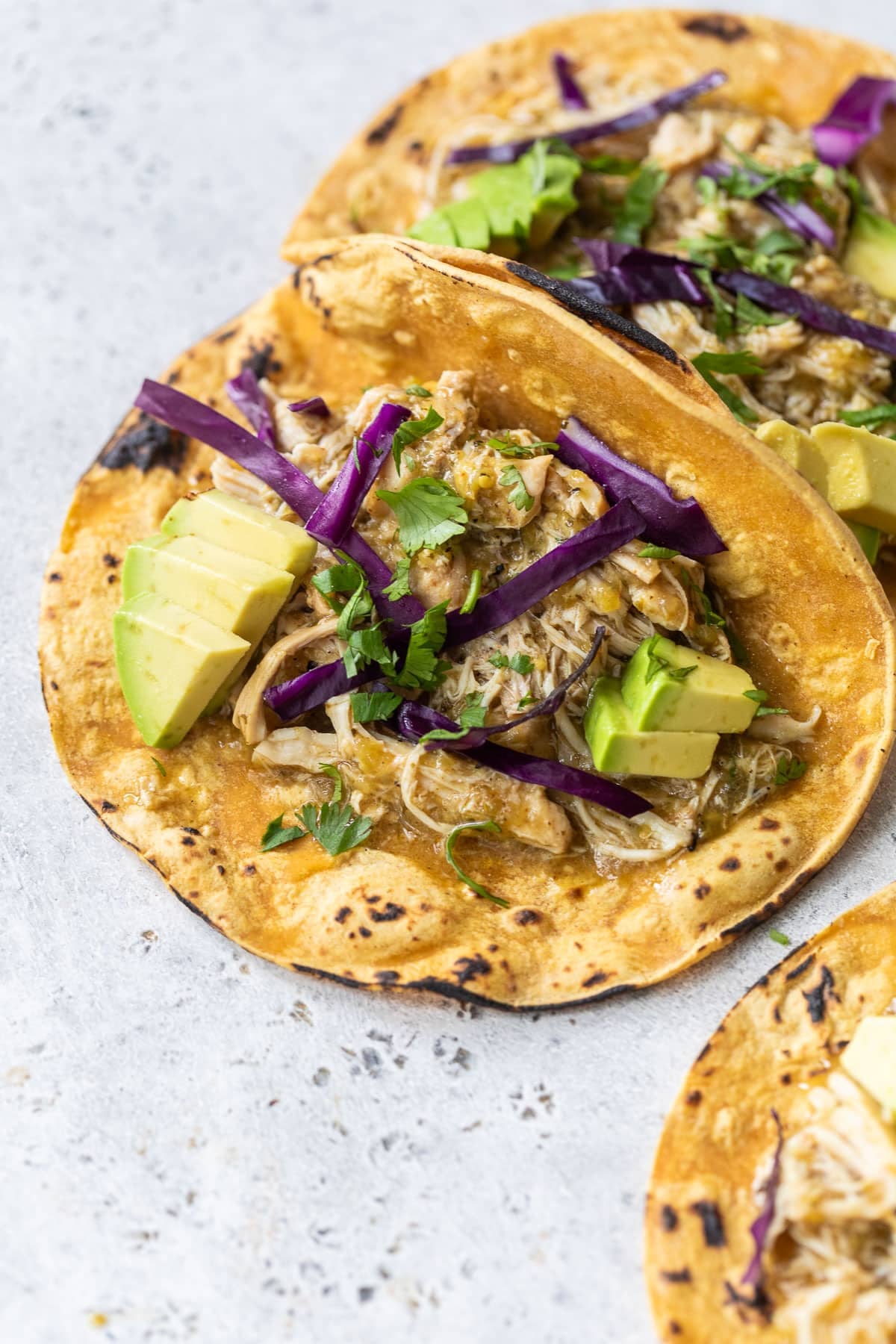 side view of salsa verde chicken taocs topped with shredded cabbage and avocado cubes.