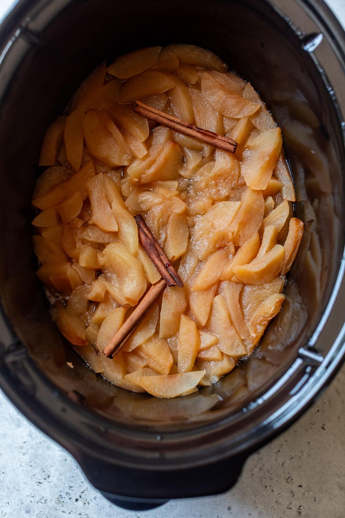 overhead view of cooked apple slices and cinnamon sticks in a slow cooker.