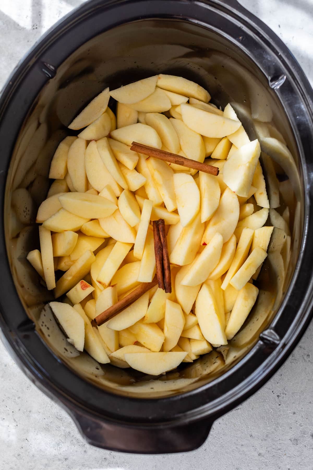 overhead view of sliced apples and cinnamon sticks in a slow cooker.