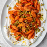 overhead view of Honey Butter Roasted Carrots topped with pistachios and served over a bed of yogurt on a serving platter.