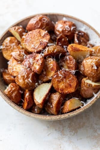 side view of a bowl full of parmesan roasted potatoes.
