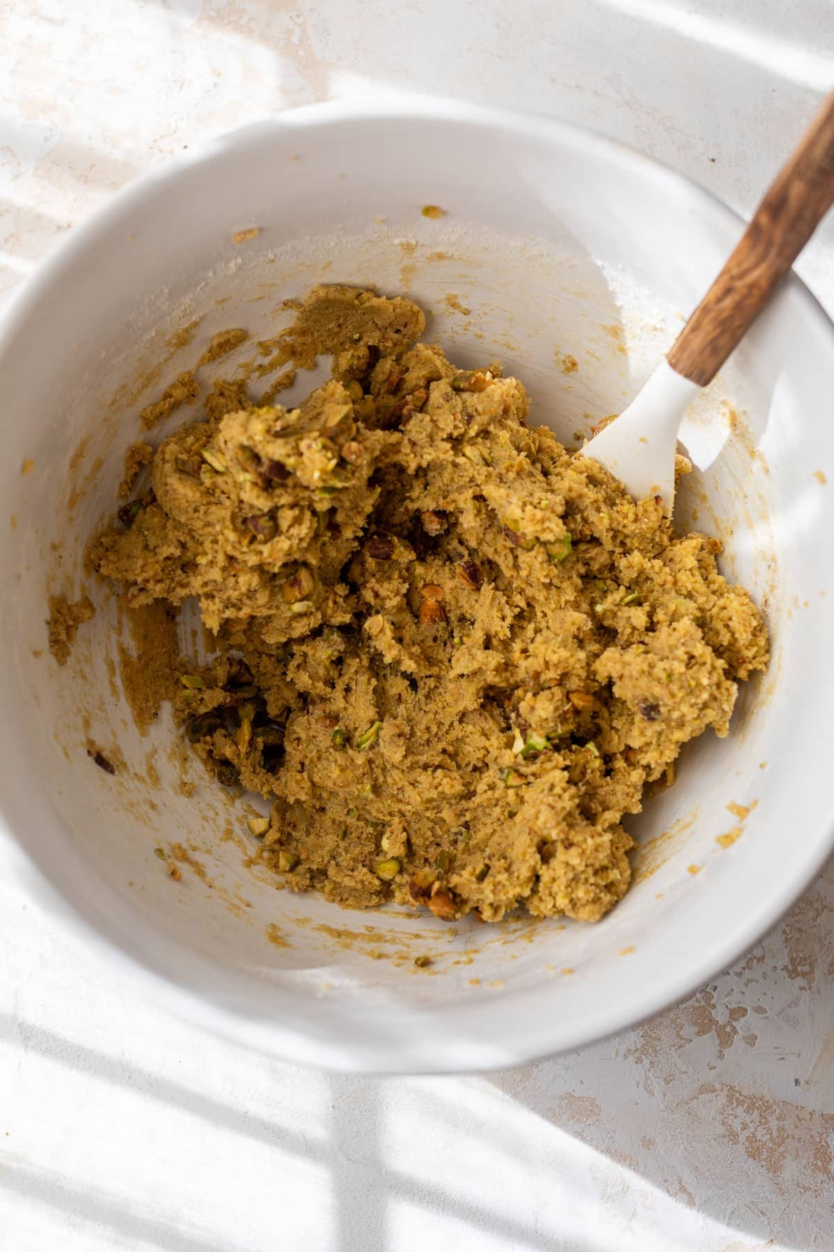 overhead view of a spatula stirring pistachio cookie dough in a large bowl.