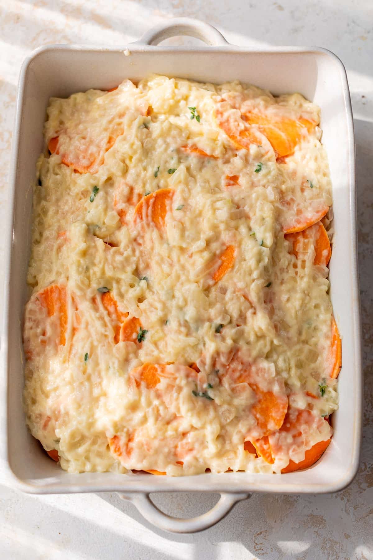 overhead view of assembled and unbaked scalloped sweet potatoes in a casserole dish.