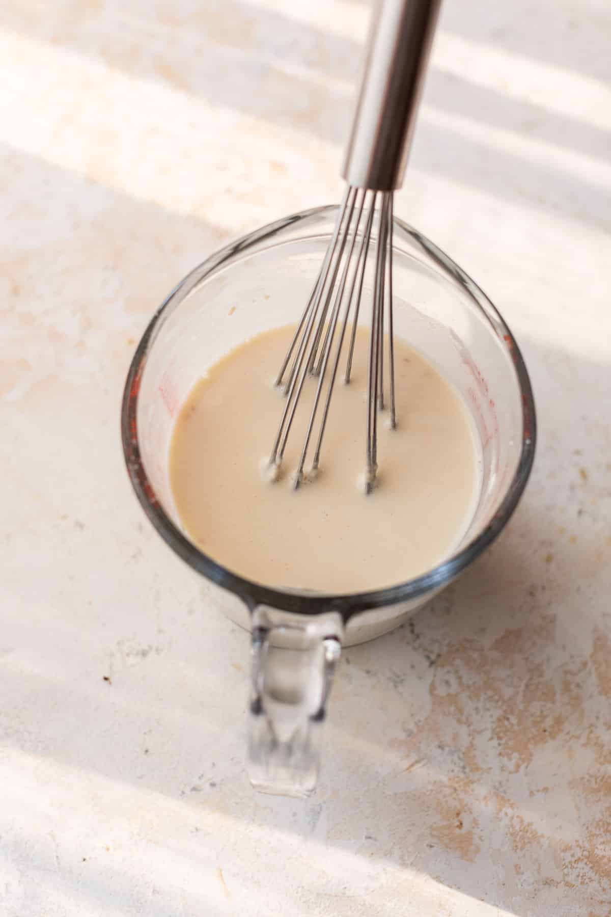 overhead view of a milk mixture being whisked in a glass measuring cup.