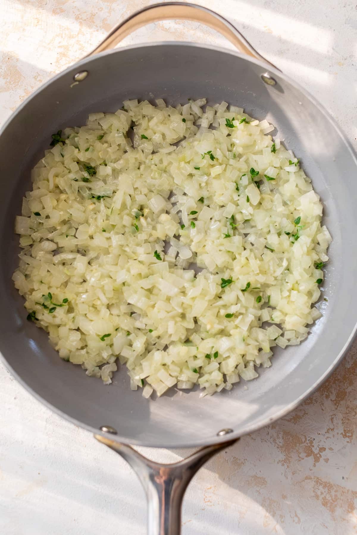 overhead view of a chopped onions and herbs cooking in a skillet.